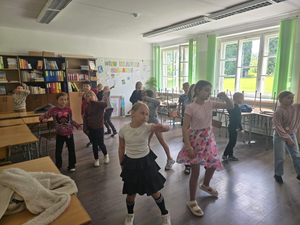 Skolēni dejo skolas bibliotēkā pie grāmatu plauktiem