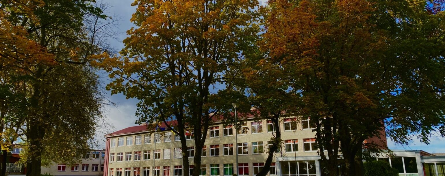 Madlienas skolas ēkas attēls ar rudenīgiem kokiem priekšplānā