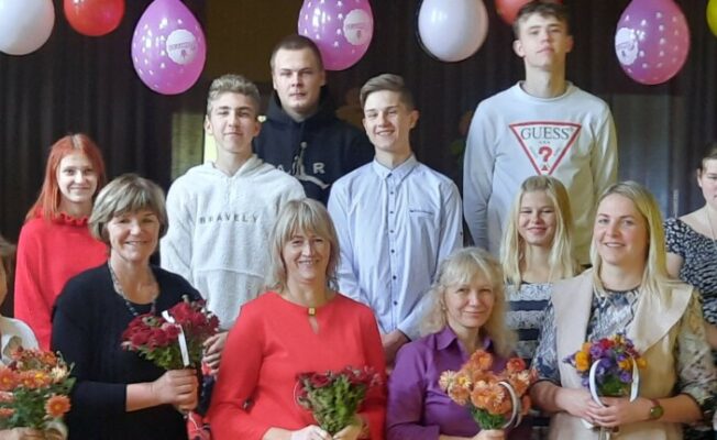 Skolas kolektīvs ar ziediem svinīgā pasākumā