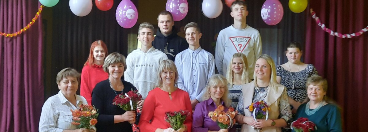 Skolas kolektīvs ar ziediem svinīgā pasākumā