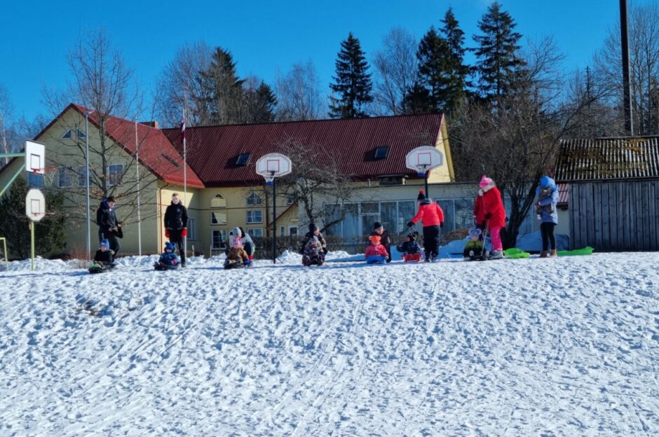 Skolēni spēlē pie skolas ziemā, fonā basketbola grozi