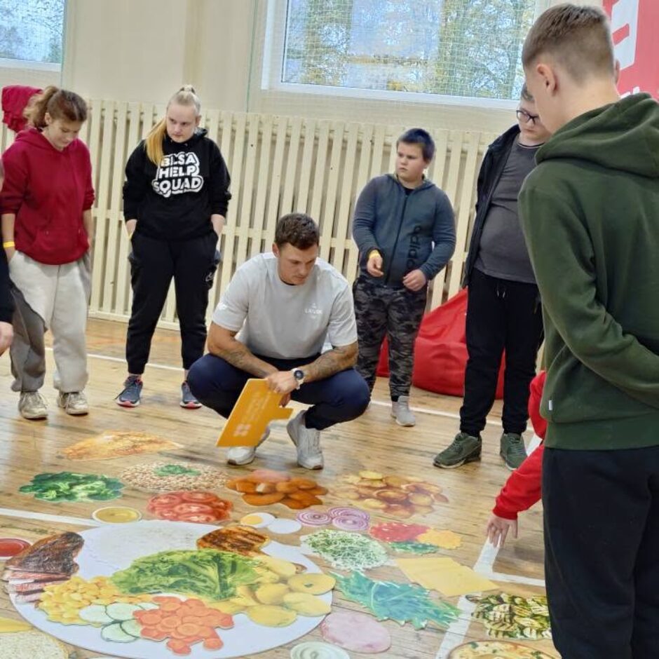 Sportists kopā ar skolēniem liek kopā veselīga uztura šķīvi