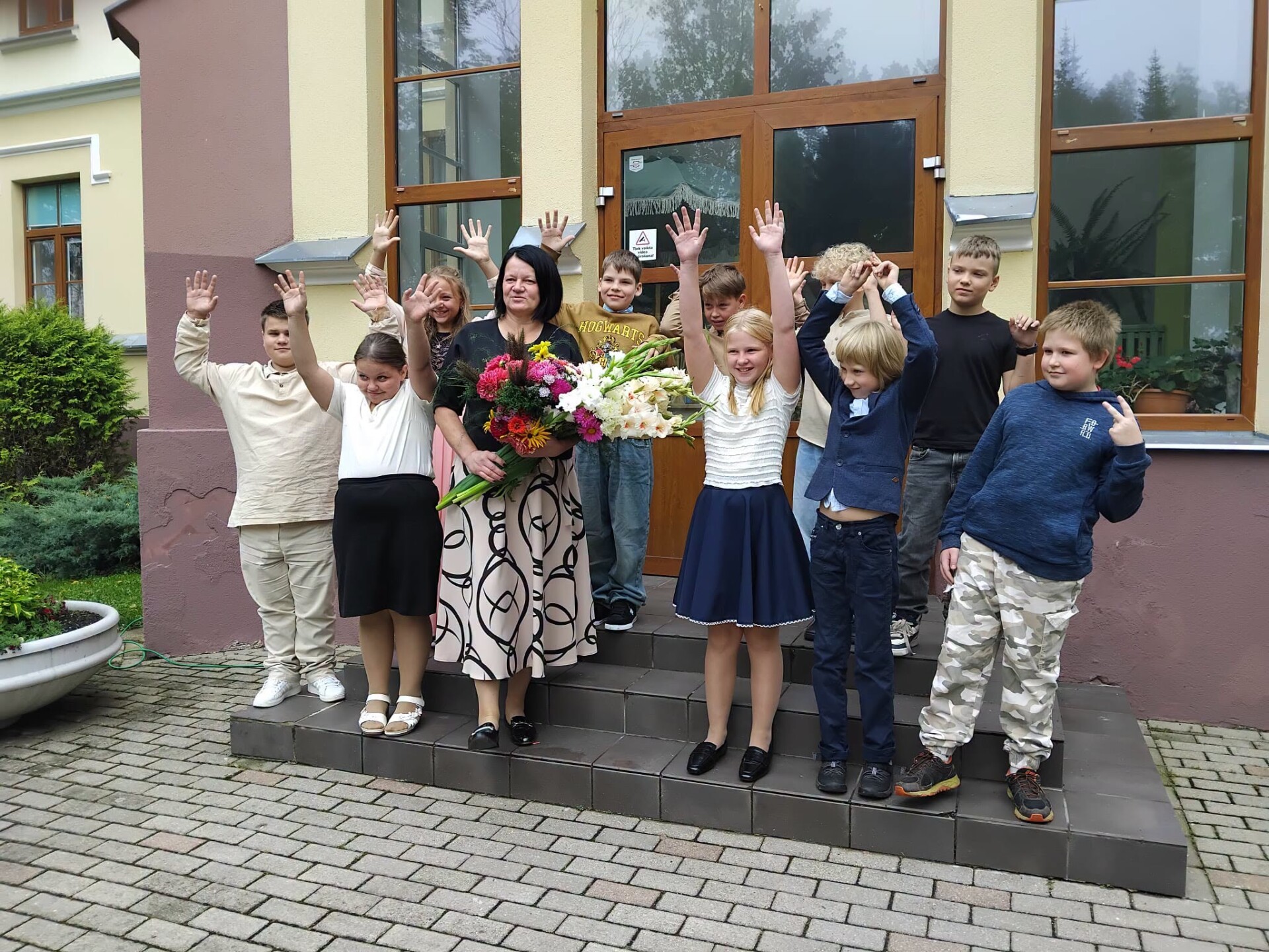 Pie skolas ēkas stāv priecīgi skolēni skolēni
