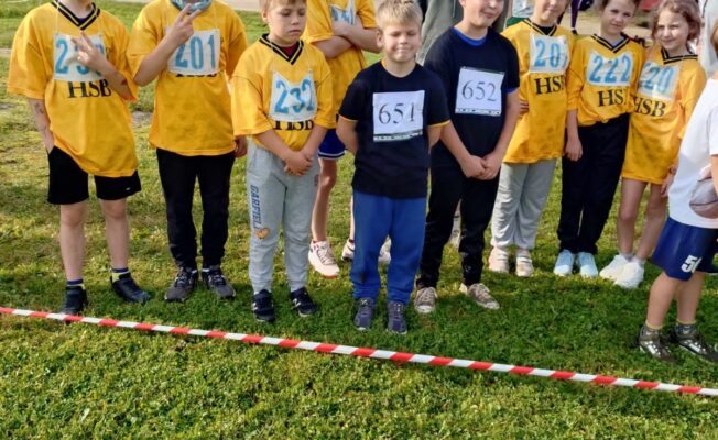 Bariņš skolēnu dzeltenos krekliņos stāv zālājā.
